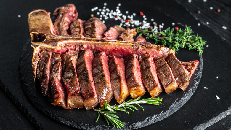 A sliced grilled porterhouse steak garnished with rosemary, thyme, and salt